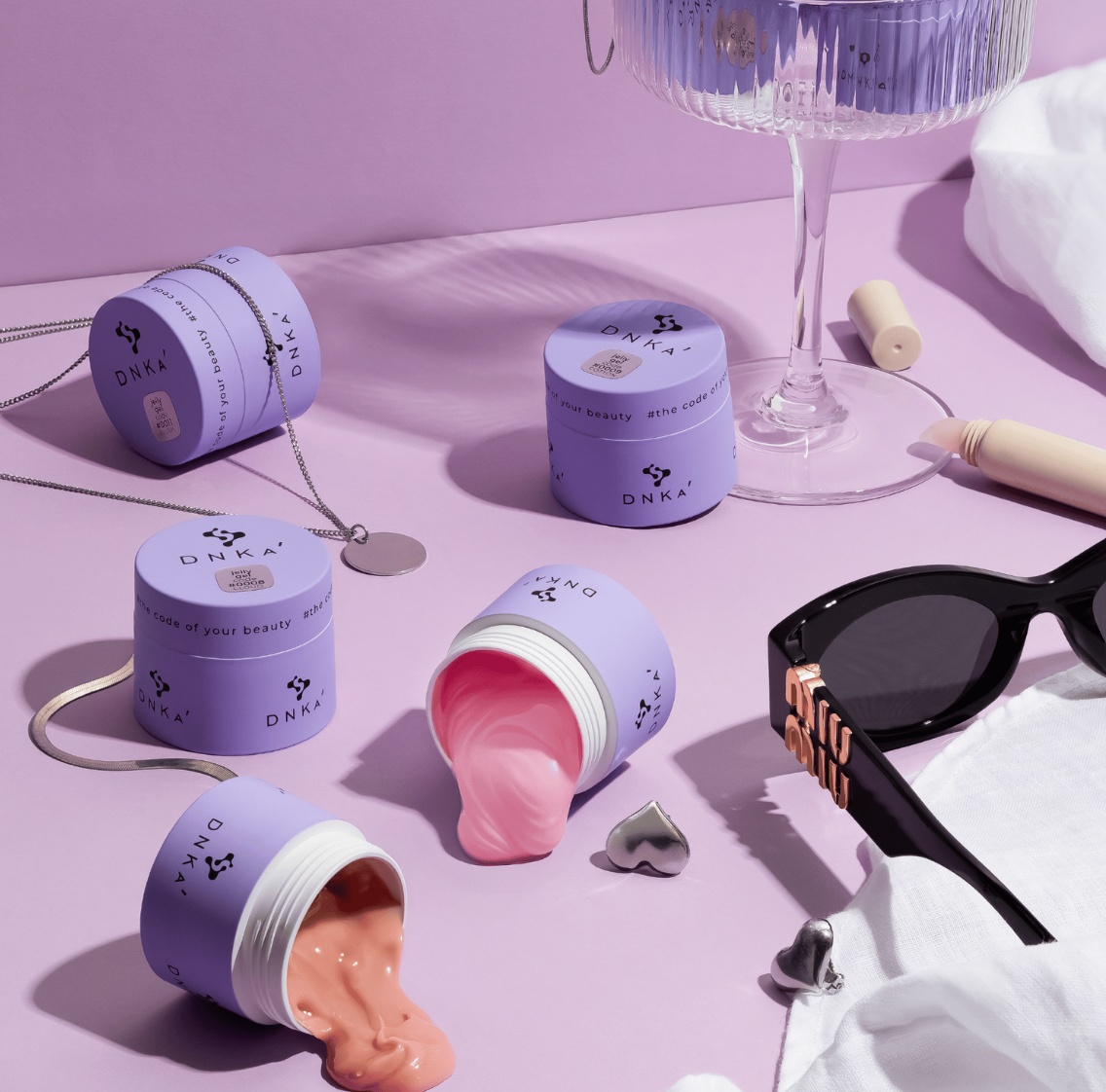Purple skincare jars with different textures on a pink surface, featuring the brand 'DNA'.