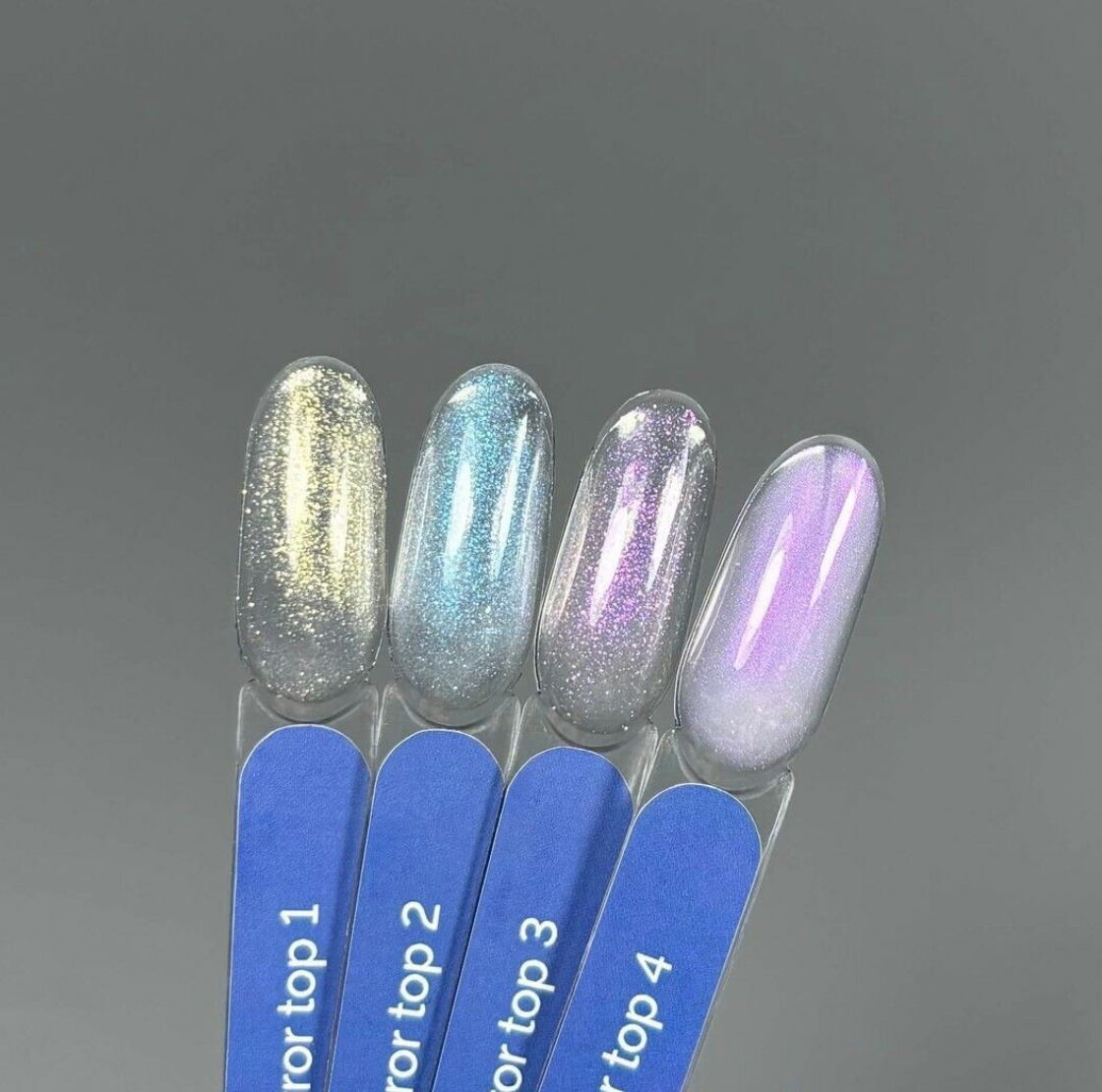 Four nail samples with different glittery nail polishes on blue sticks against a gray background