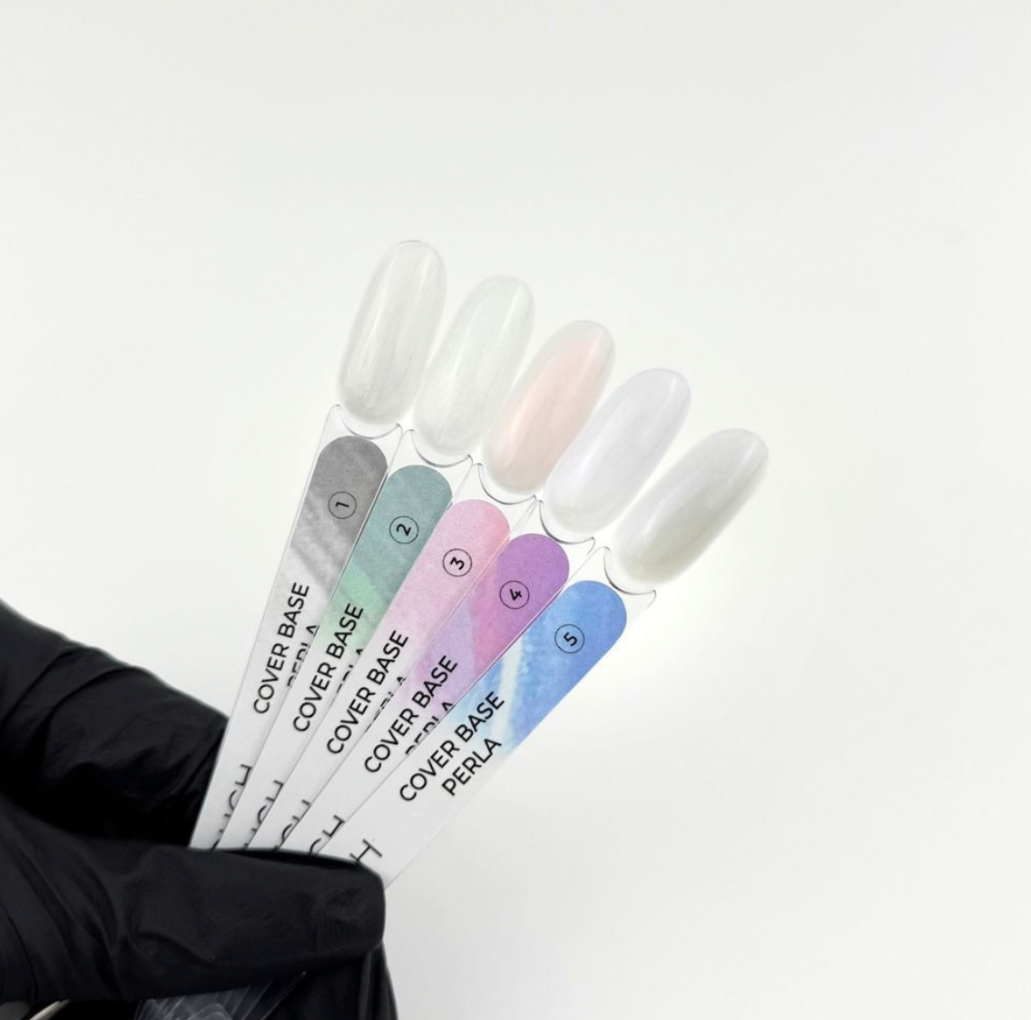 Set of nail polish bottles with gradient colors held by a gloved hand on a white background