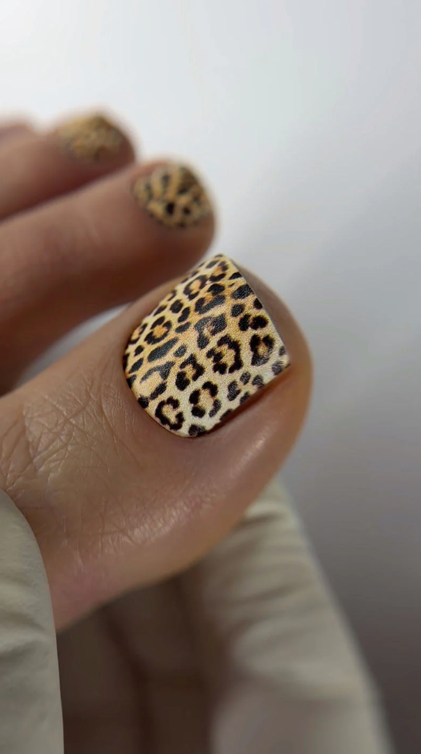Close-up of a hand with leopard print nail polish on a neutral background