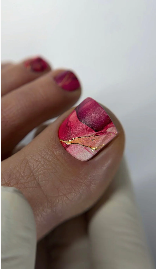Nail with pink and gold marbled design on a white background