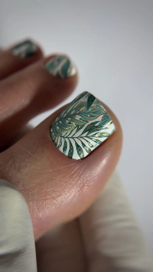 Close-up of a hand with a leaf-patterned nail design on a plain background