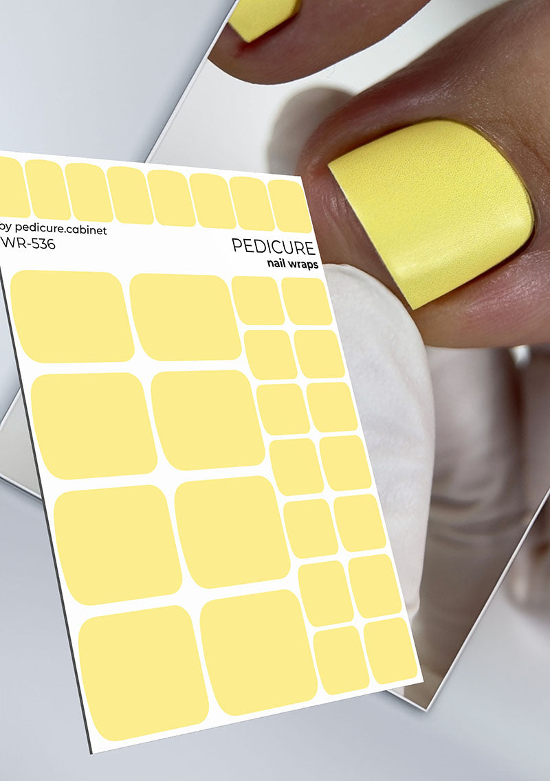 Sheet of yellow pedicure nail wraps with a person wearing a yellow nail wrap on their finger.