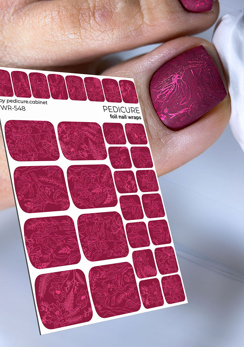 Sheet of pink nail wraps held by a hand with pink nail polish on a light gray background
