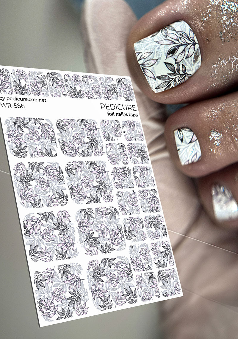 Foil pedicure nail wraps with leaf design held by a hand with similarly designed nails.