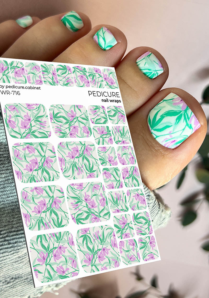 pedicure nail wrap sheet with floral design held by a hand with matching nails.