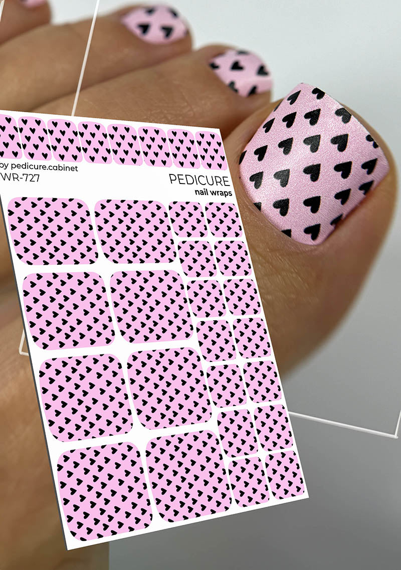 Pink pedicure nail wraps with black heart pattern on a white background