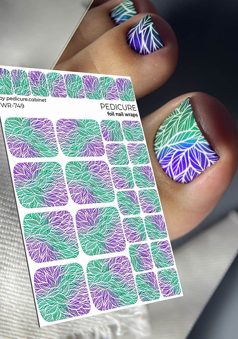 Foil nail wraps with purple and green leaf pattern on a pedicure cabinet, with a hand showing nails with similar design.