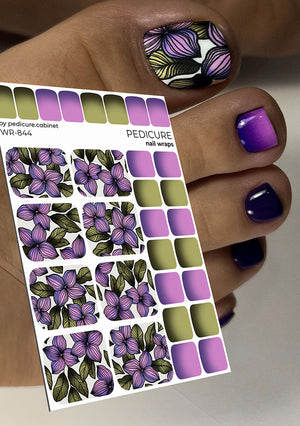 Nail wrap sheet with purple and green floral design held by a hand with matching nails.