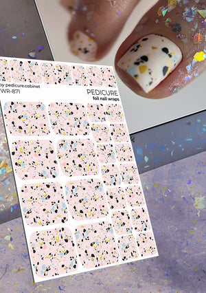Sheet of foil nail wraps with a terrazzo pattern, next to a hand with decorated nails.