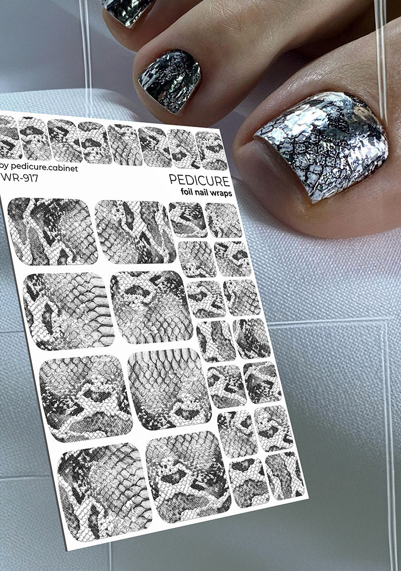 Sheet of foil nail wraps with snake skin pattern next to a hand with silver and black patterned nails.