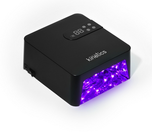 A black Kinetics UV/LED nail lamp with a digital display on top and a glowing purple light output, shown on a white background.