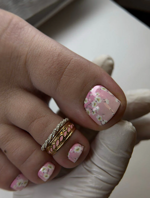 Hand with pink floral nail design wearing a gold ring on a neutral background