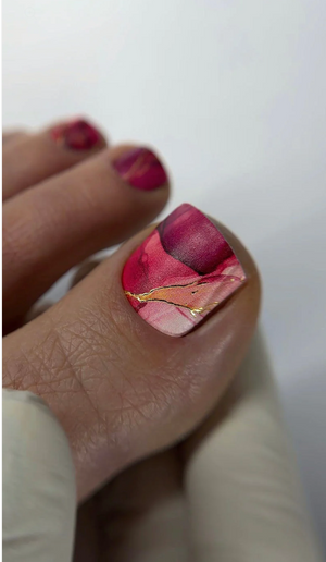 Nail with pink and gold marbled design on a white background