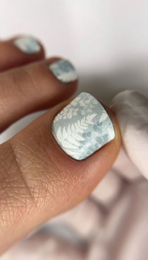 Close-up of a hand with a silver square earring and matching nail design.