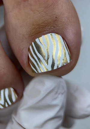 Nail with gold and white striped design on a neutral background