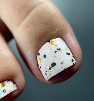 Nail with terrazzo design and gold accents on a neutral background